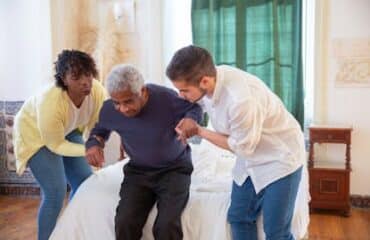 A-Man-and-a-Woman-Assisting-an-Elderly-Man-in-Standing
